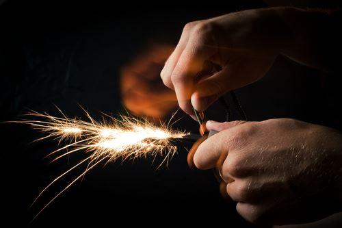 Close-up of hands using a firestarter to create sparks in a dark setting