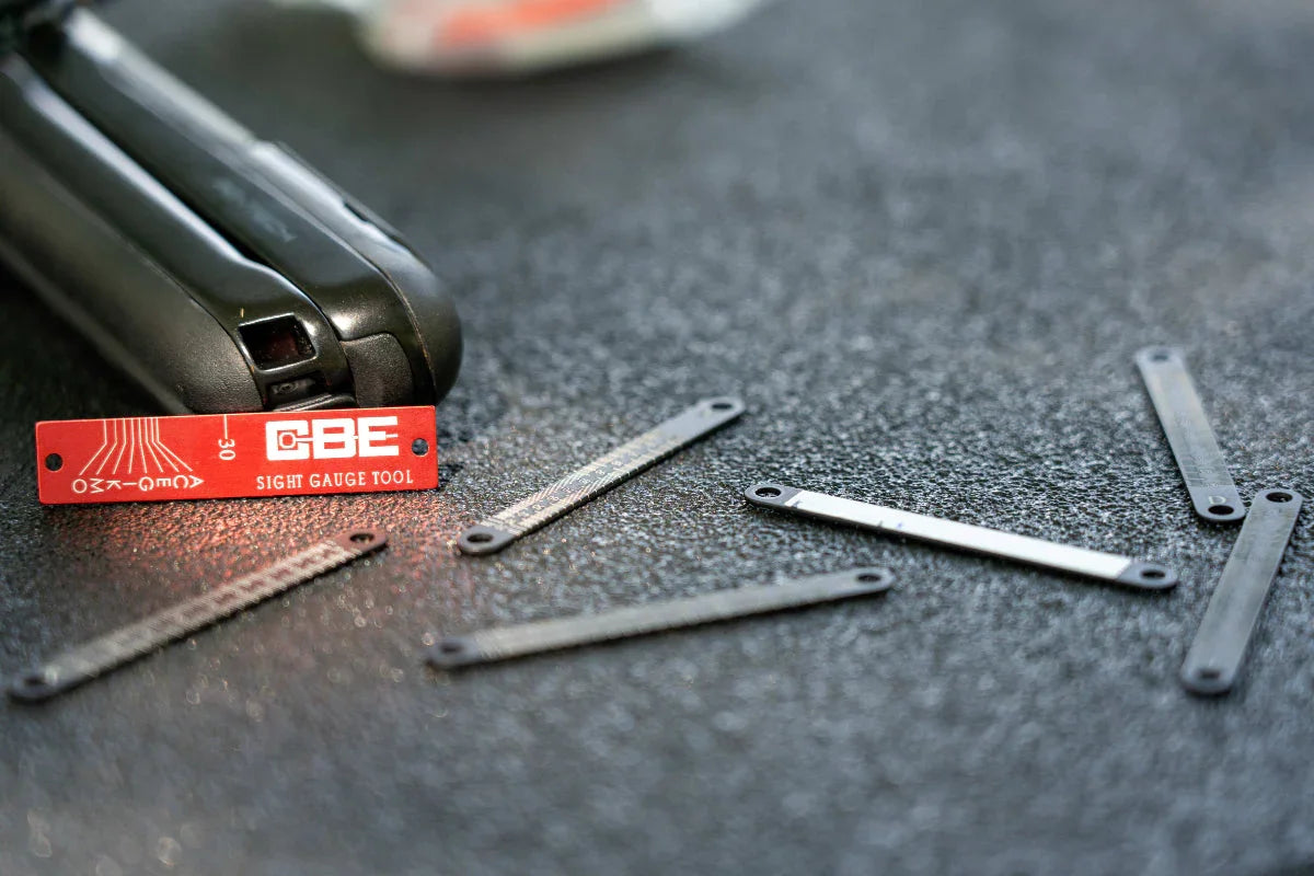CBE sight gauge tool and metal strips on textured black surface.