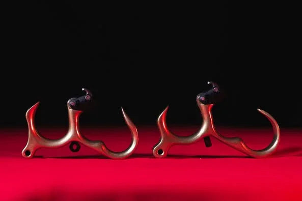 Two metallic archery release aids with finger grips on a red surface and black background
