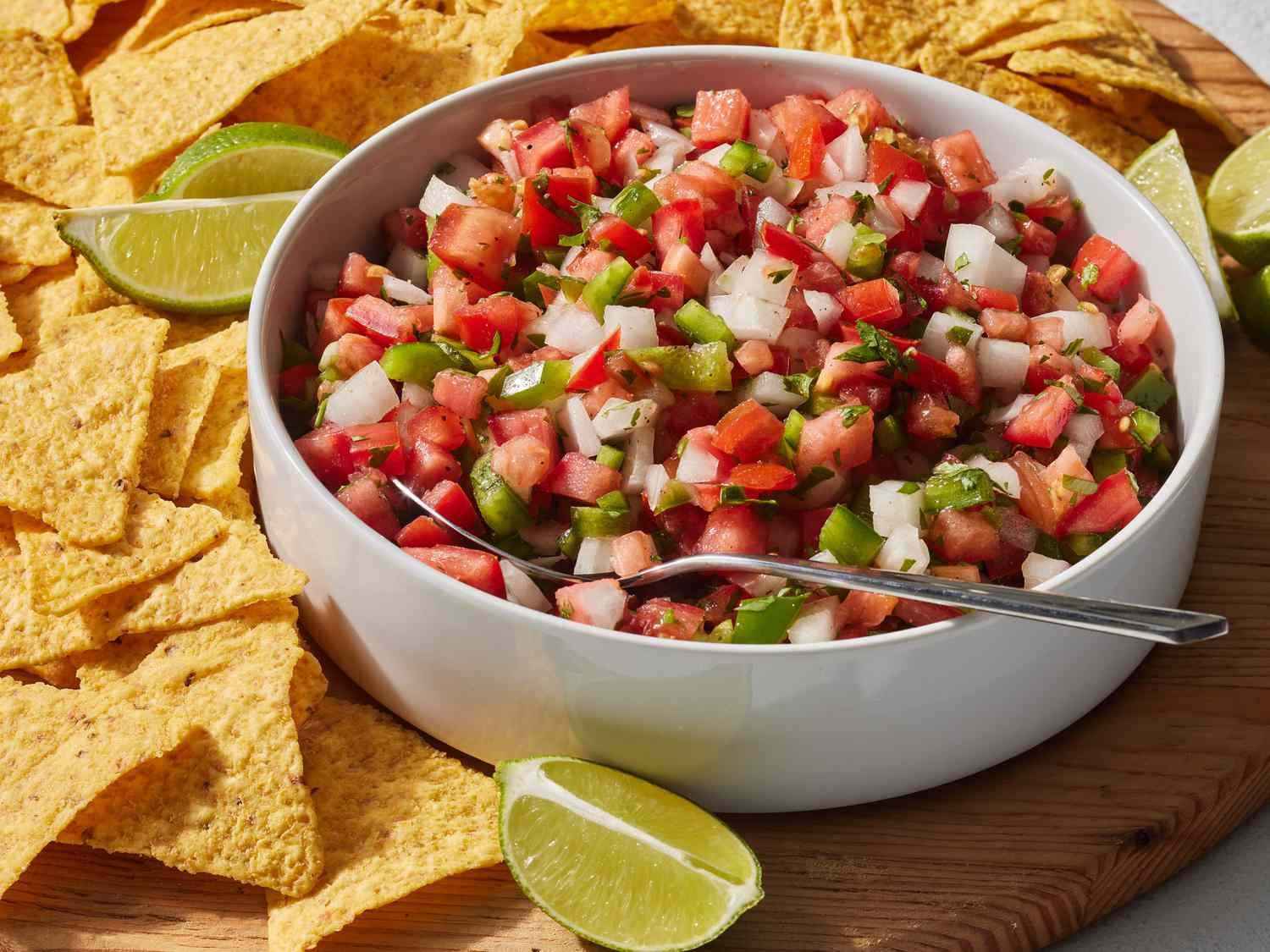 Fresh tomato salsa in a white bowl surrounded by tortilla chips and lime wedges