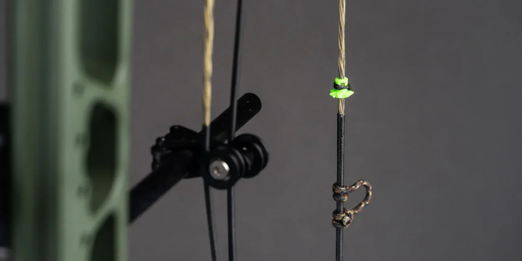 Compound bow string close-up with green nocking points and black serving against a gray background