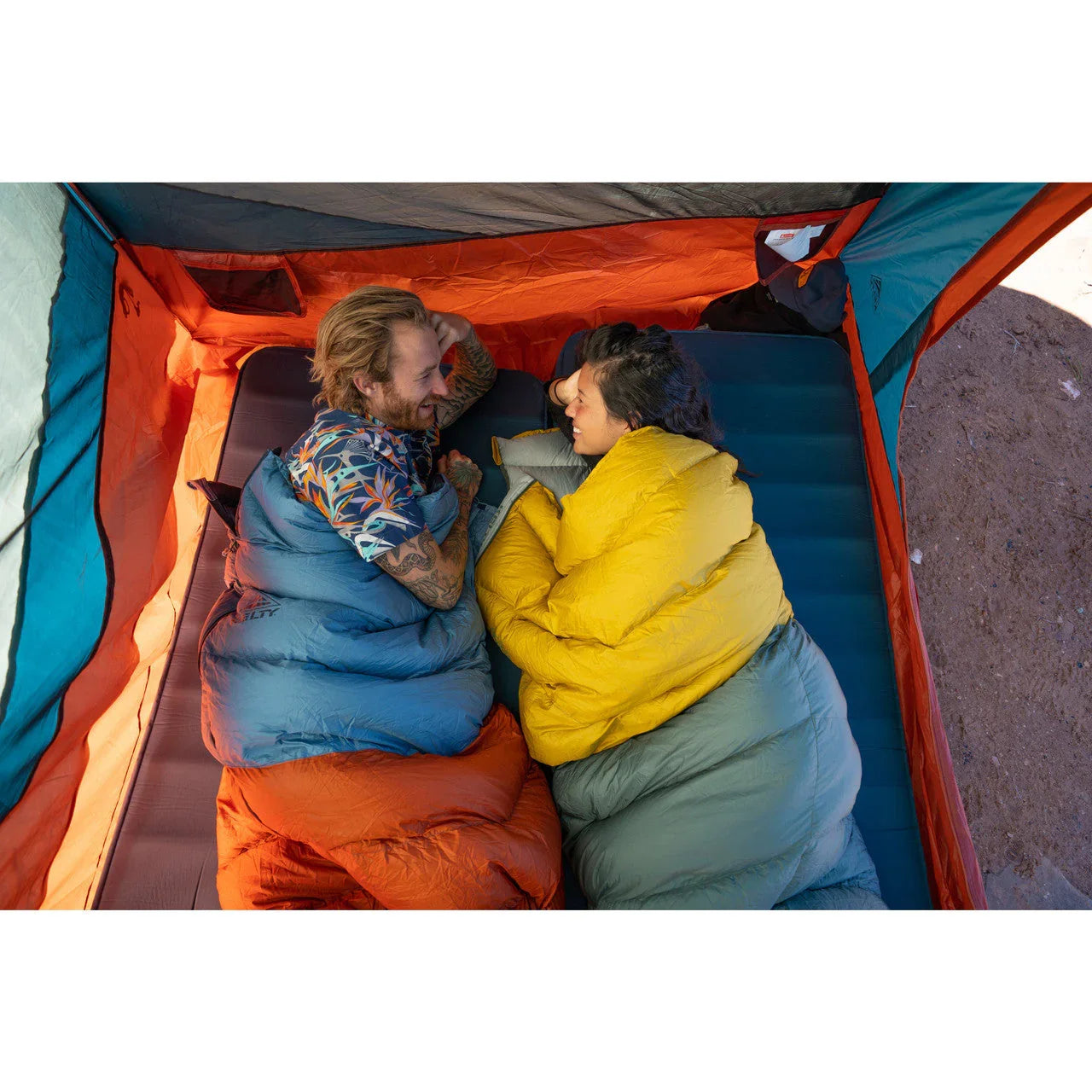 Couple in sleeping bags camping inside orange and blue tent on air mattress