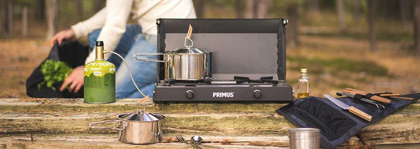 Camping gas stove Primus with pots and utensils on a log in a forest setting