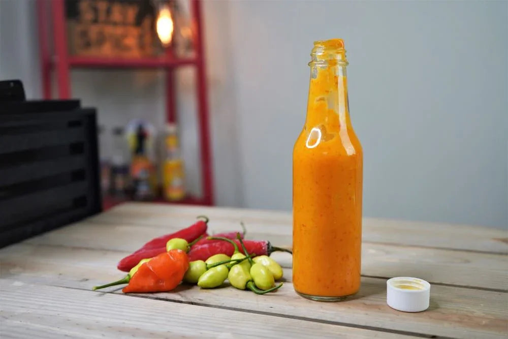 Homemade habanero hot sauce in a glass bottle with fresh peppers on wooden table