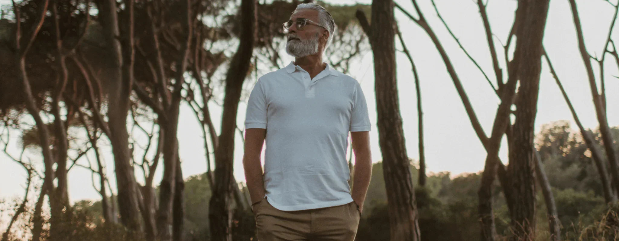 Man in a white polo shirt and khaki pants outdoors with trees in the background