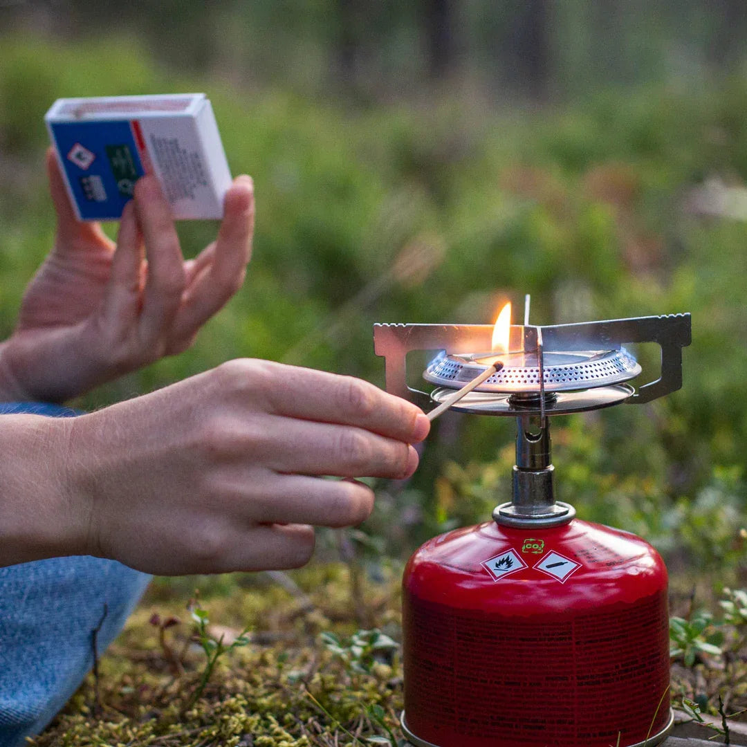 Lighting a camping gas stove outdoors with a match and red fuel canister