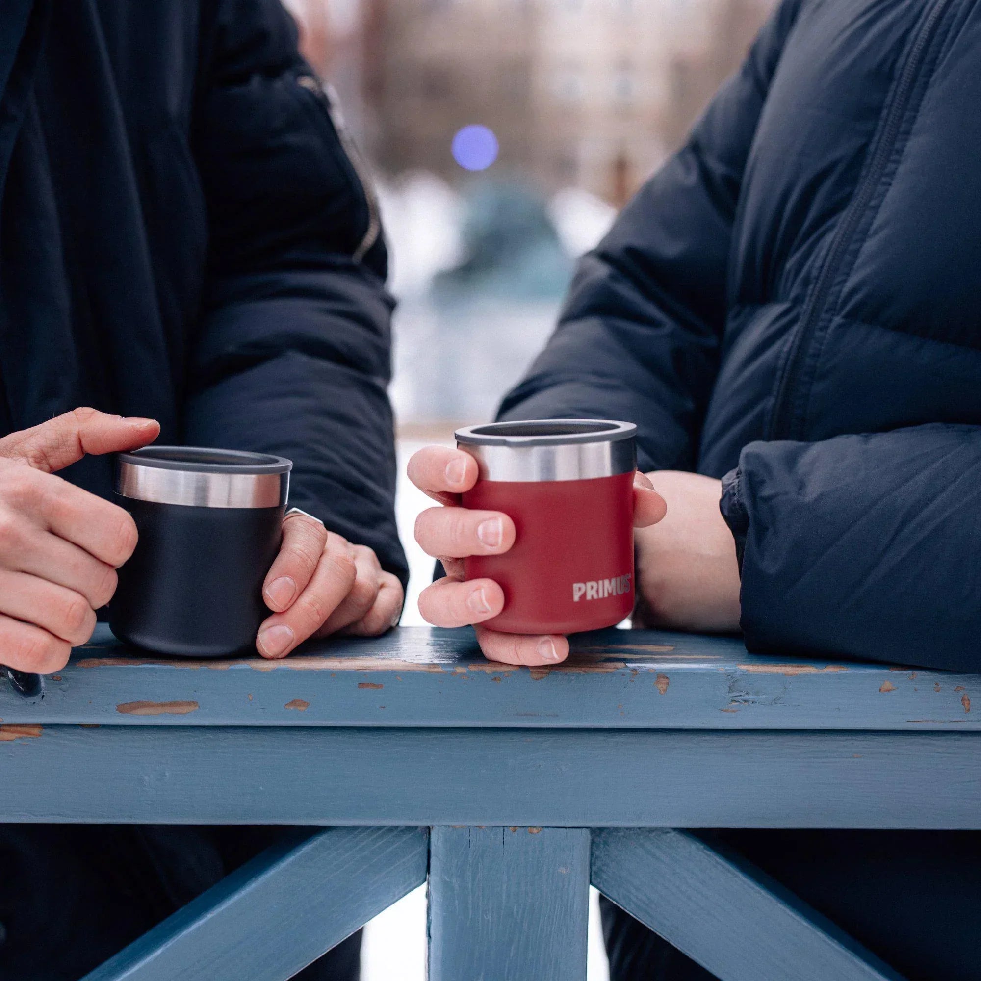 Two people in winter jackets holding Primus insulated cups outdoors in cold weather.
