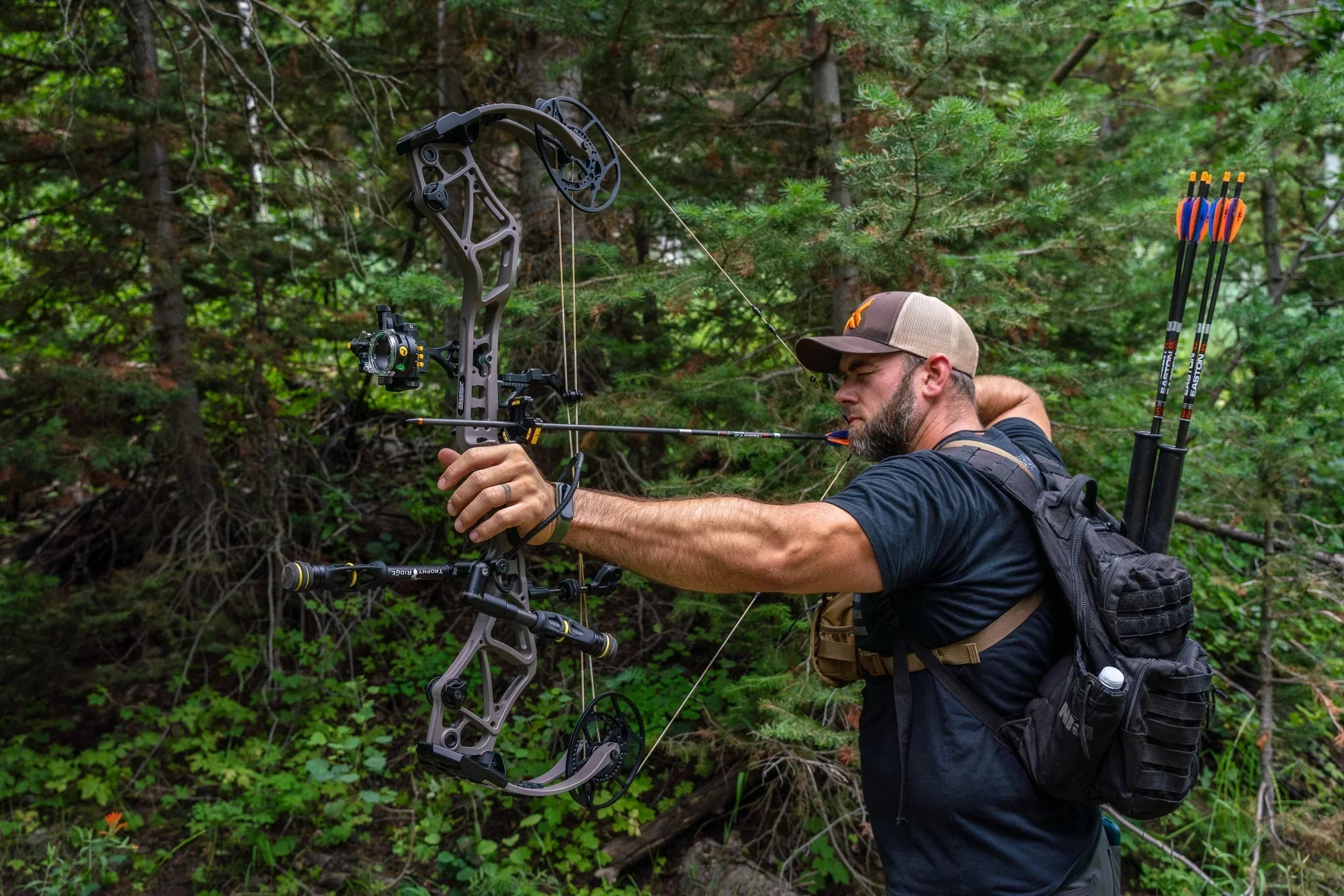 Man aiming compound bow in forest, archery backpack with arrows, outdoor hunting gear