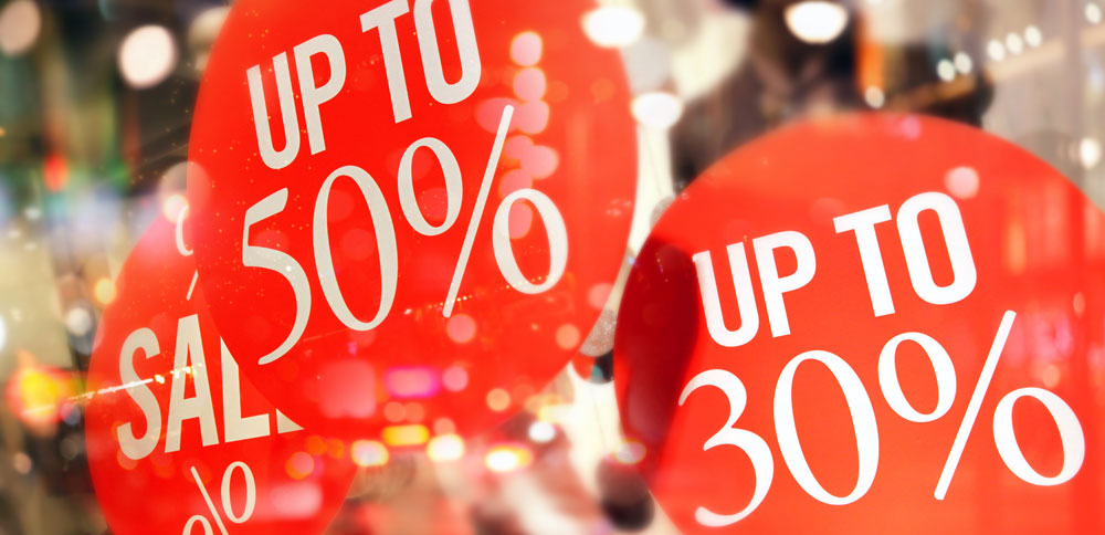 Red sale signs with bold white text up to 50% off and up to 30% discount in store window