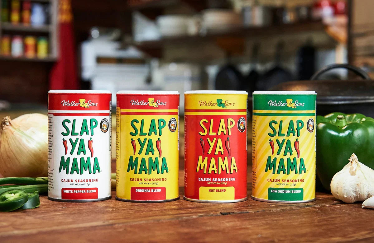 Slap Ya Mama Cajun seasoning containers beside grilled meat, seafood, and Louisiana-style cooking