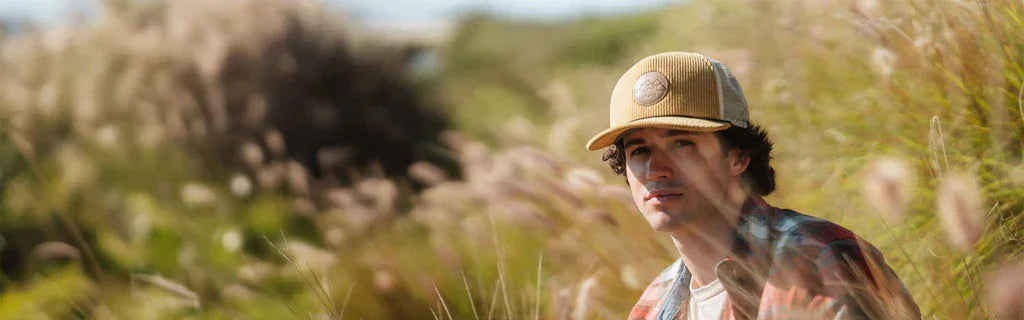 Man in beige trucker hat and plaid shirt outdoors in tall grass field