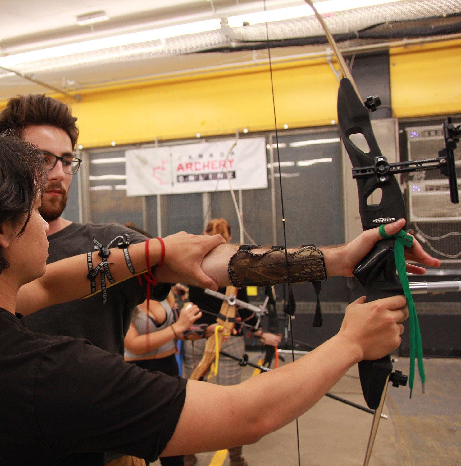 Archery instructor teaching student to aim with recurve bow at indoor archery range
