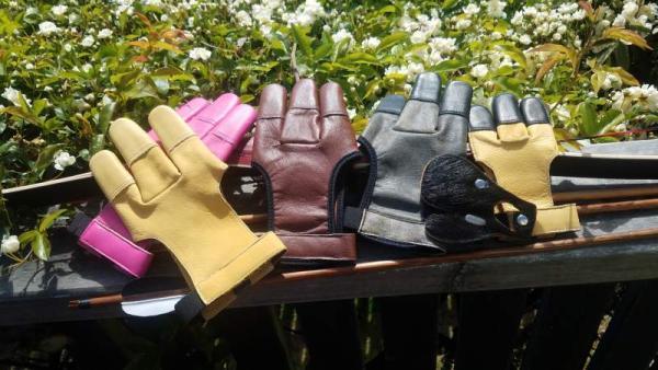Assorted archery gloves in pink, brown, grey, and yellow on wooden fence outdoors