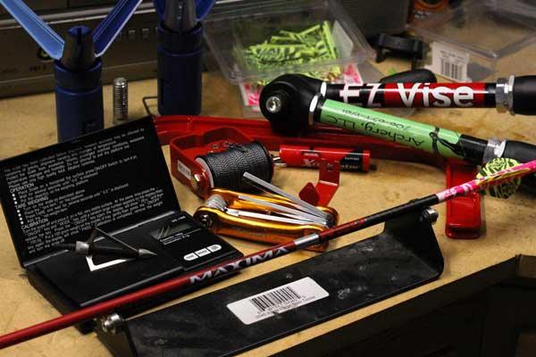 Assorted archery tools and arrow shaft on workbench, including vise and nocks
