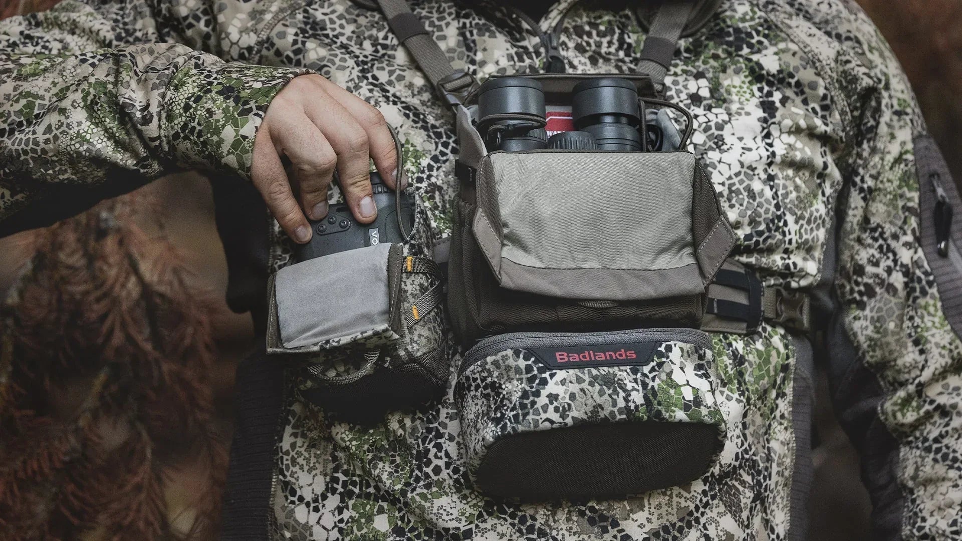 Hunter in camo gear wearing Badlands chest pack and holding rangefinder outdoors