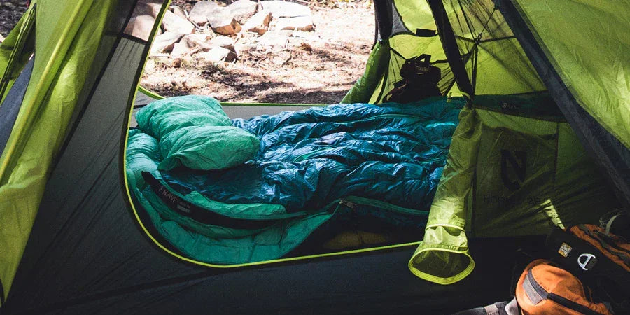 Blue backpacking sleeping bag inside green tent at outdoor campsite