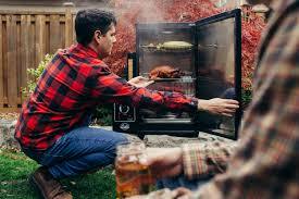 Man in plaid shirt using outdoor electric smoker in backyard grill setting