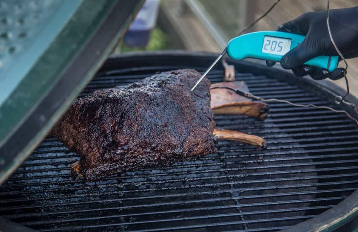 Smoked beef ribs on grill with meat thermometer showing 205 degrees for barbecue cooking
