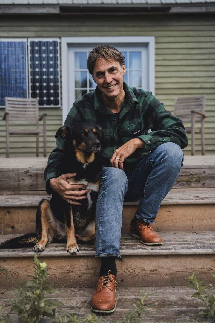 Man in green plaid flannel shirt and jeans sitting on outdoor steps with a dog