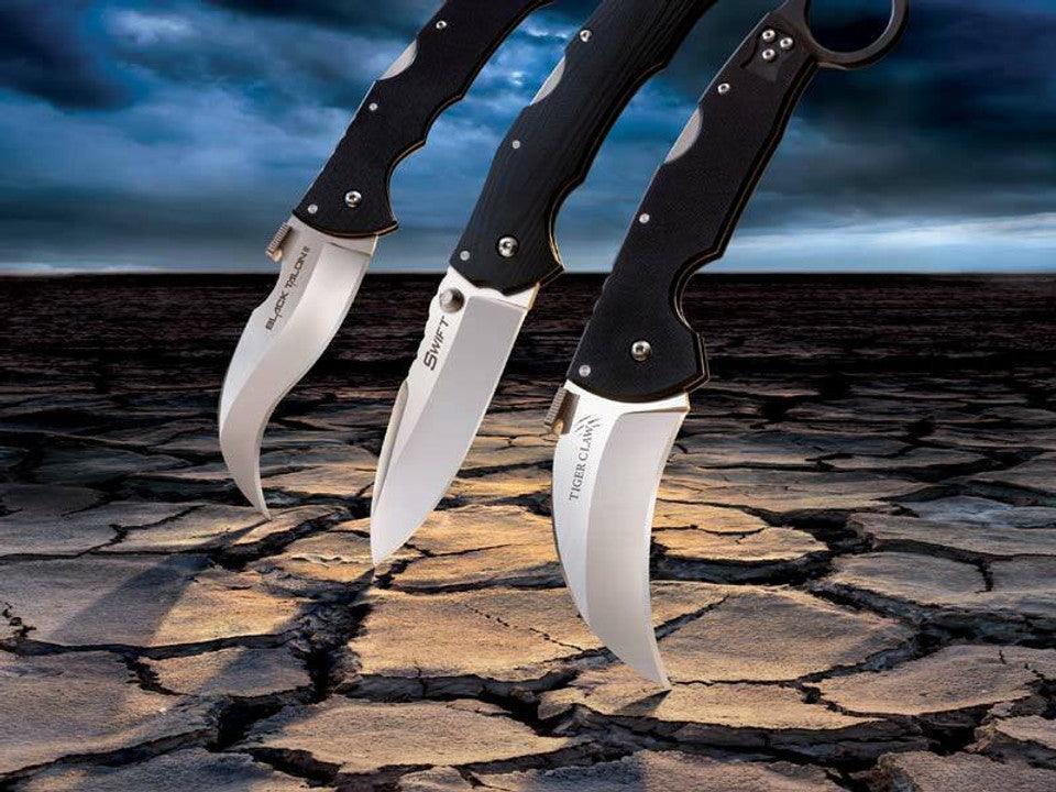 Three folding knives with curved blades on cracked earth under dramatic cloudy sky