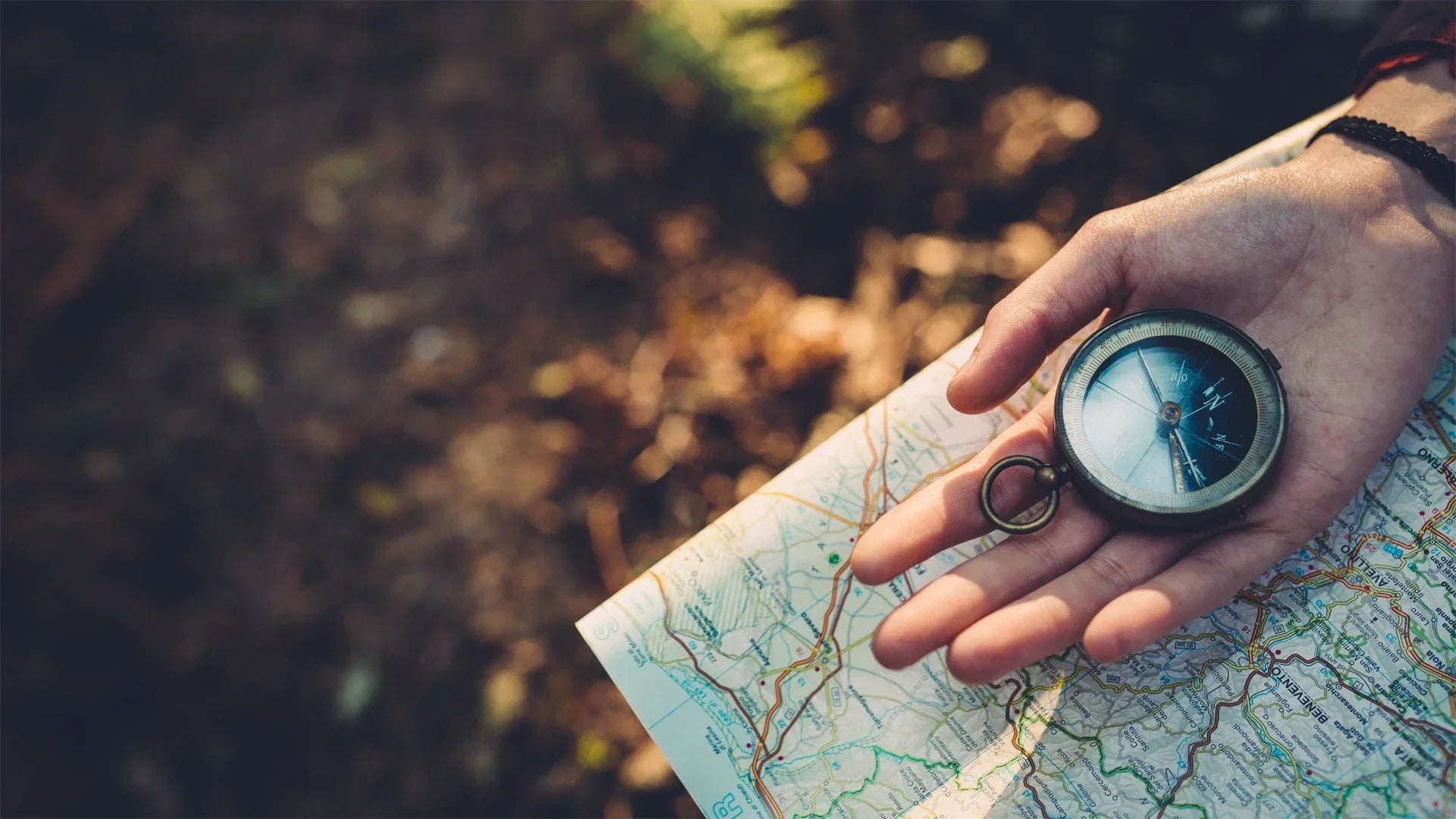 Hand holding a compass over a detailed road map outdoors, navigation and adventure concept