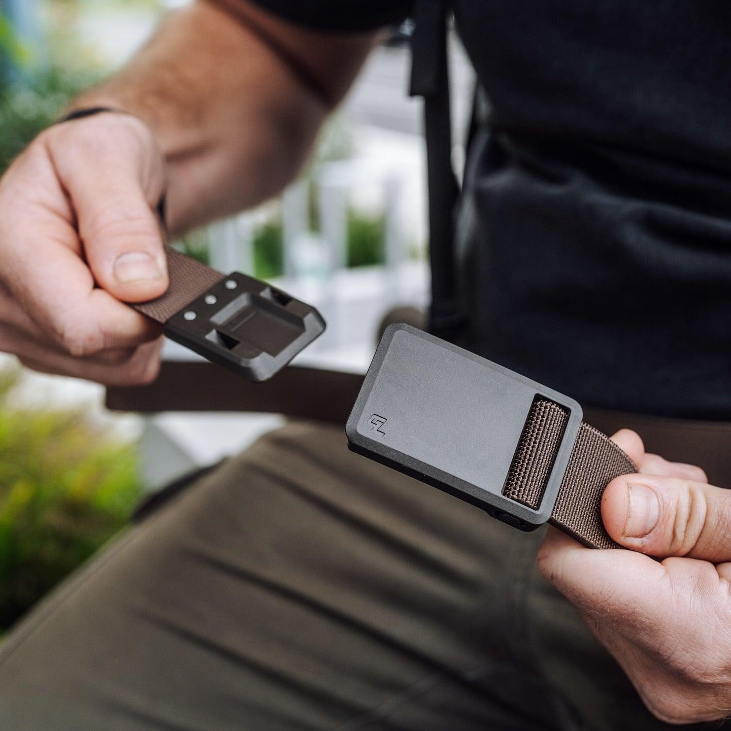 Man holding brown tactical belt with rectangular magnetic buckle outdoors