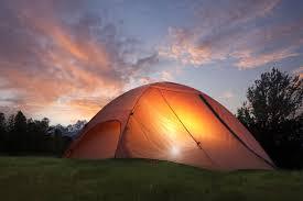 Glowing orange camping tent on grass at sunset with trees and cloudy sky