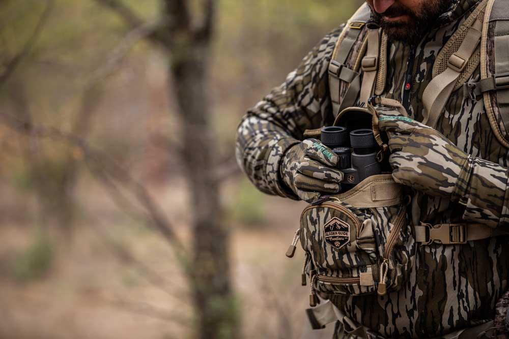 Hunter in camouflage gear with binoculars and Alaska Guide Creations chest pack outdoors