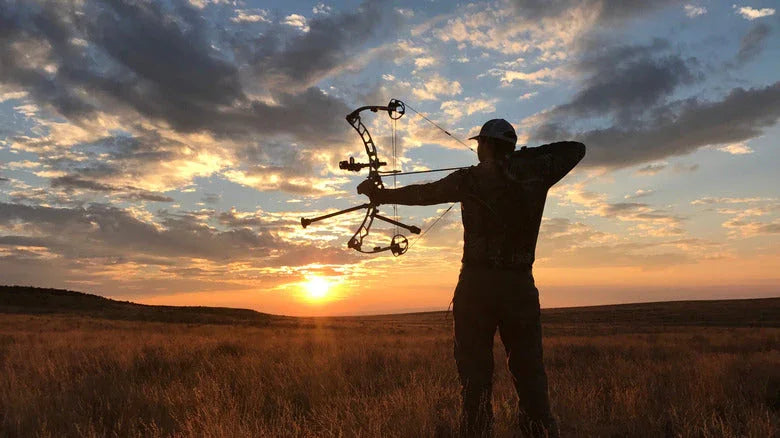 Silhouette of an archer with a compound bow aiming at sunset in an open field