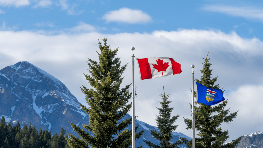 Canadian and Alberta flags flying with pine trees and mountains in the background