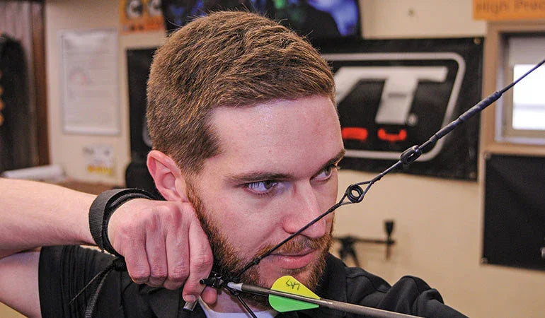 Man aiming a compound bow indoors with misaligned peep sight, archery shop setting.