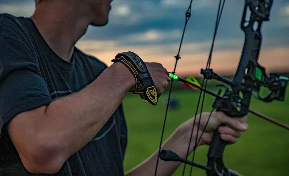 Archer aiming compound bow with green Nockturnal lighted nock outdoors at dusk