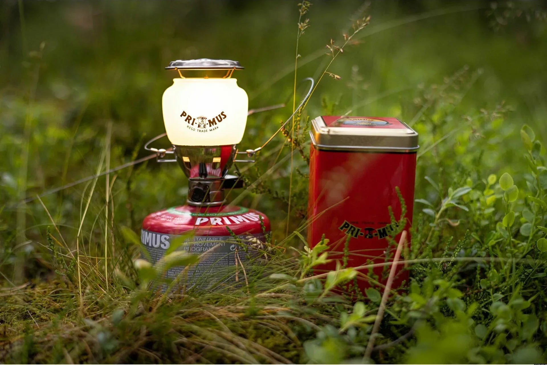 Primus camping lantern and red Primus fuel canister on grass outdoors