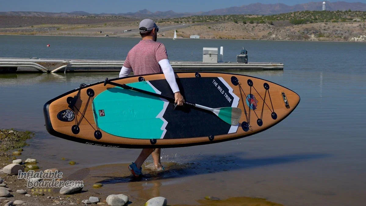 Man carrying Sequoia 11 green inflatable paddleboard by lake shore
