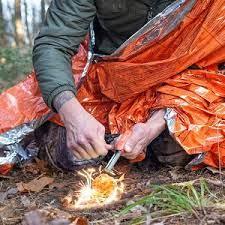 Person using fire starter outdoors wrapped in orange emergency survival blanket