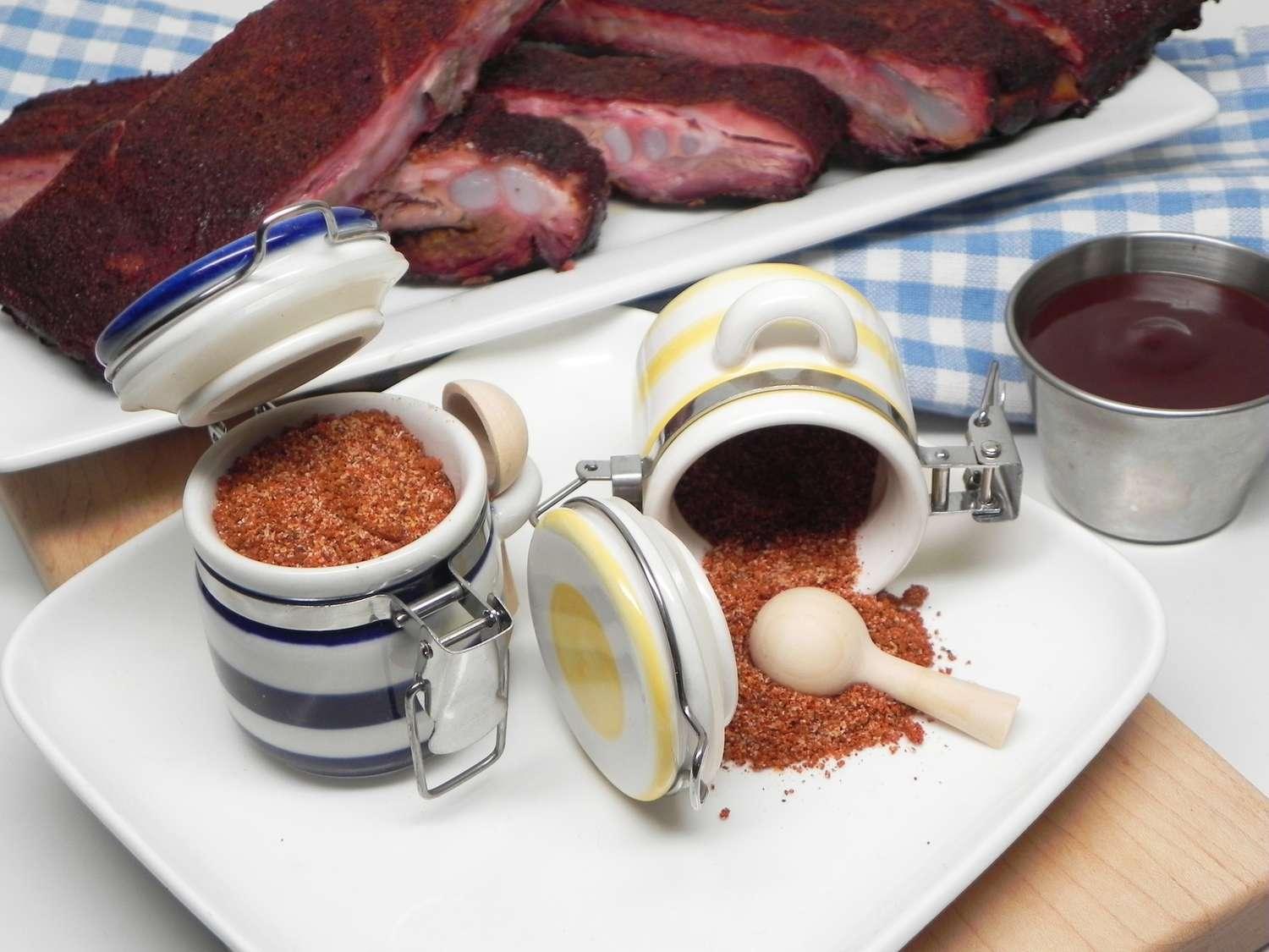 Spare rib rub spice in ceramic jars with barbecue ribs and sauce on a white plate