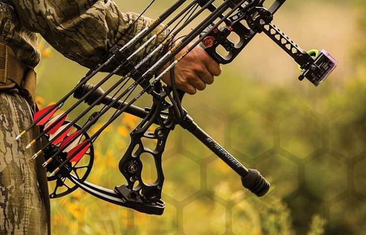 Hunter holding compound bow with stabilizer, arrows, and sights outdoors