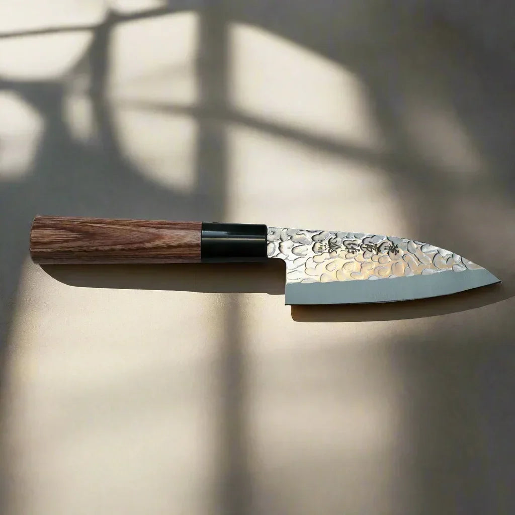 Japanese hammered steel kitchen knife with wooden handle on neutral surface