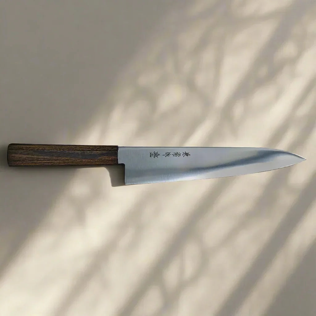 Japanese-style kitchen knife with wooden handle and engraved blade on a beige surface with shadow patterns