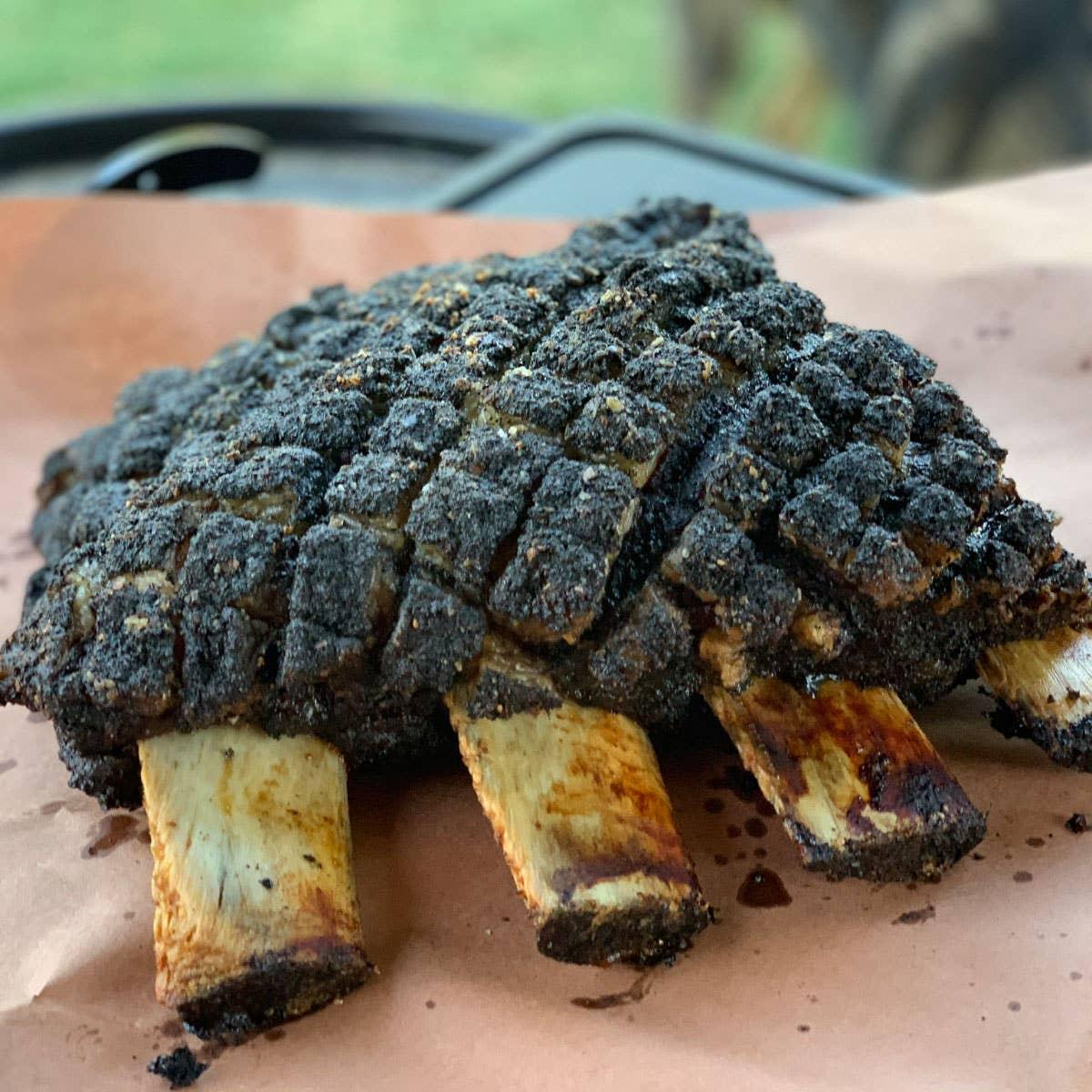 Smoked beef ribs with cracked black pepper bark on butcher paper, outdoor setting
