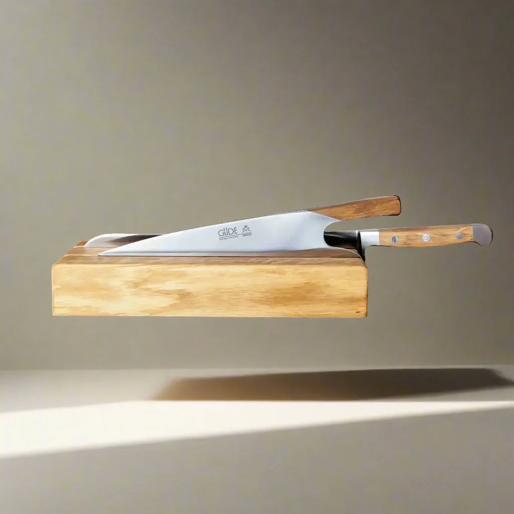 Stainless steel kitchen knives with wooden handles in a wooden knife block on neutral background.