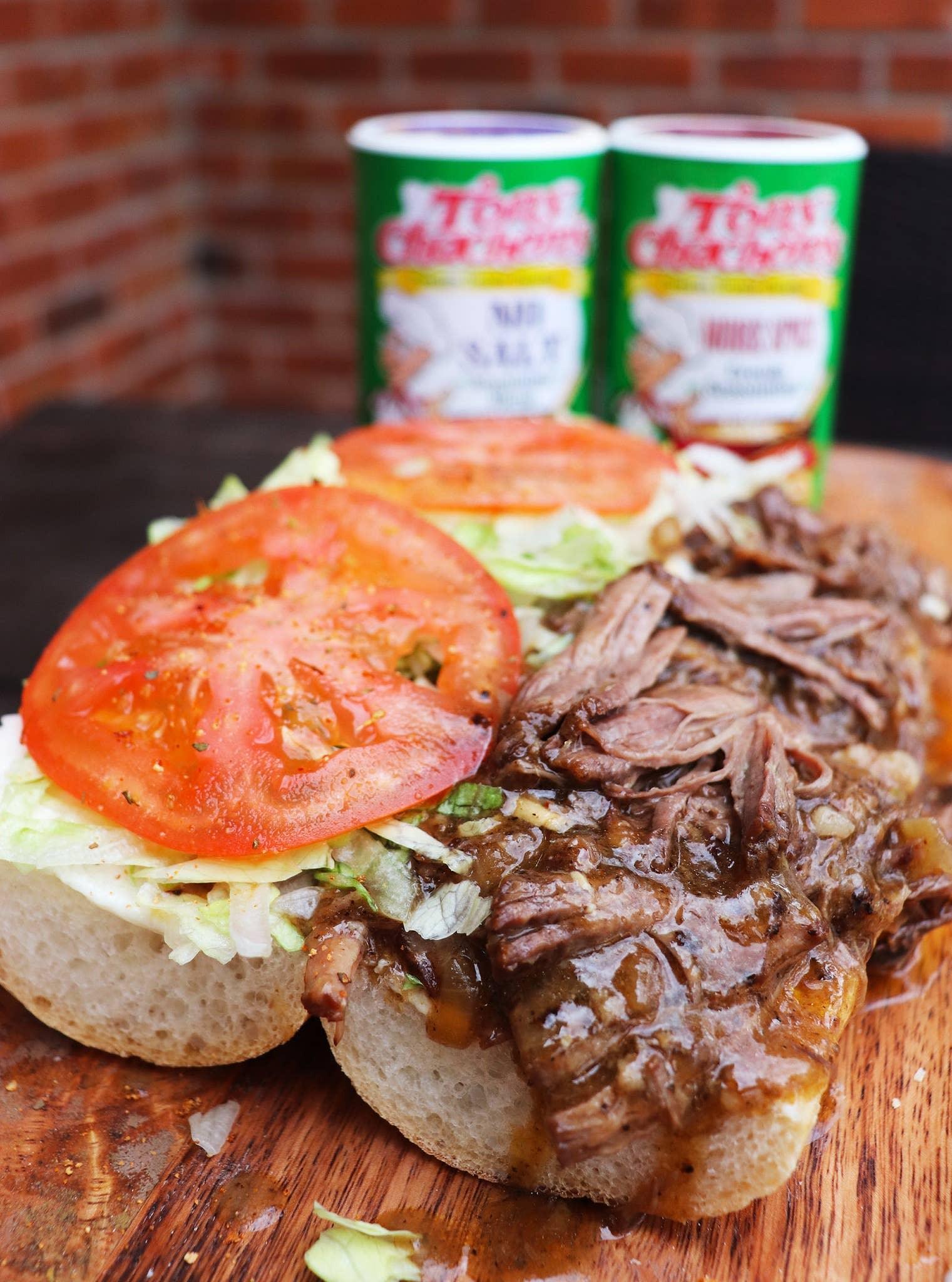 Shredded beef sandwich with lettuce, tomato, and gravy on crusty bread, outdoor setting