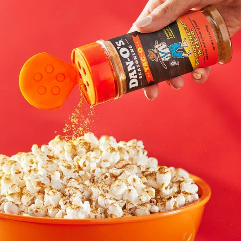 Hand sprinkling seasoning over popcorn in an orange bowl with vibrant red background
