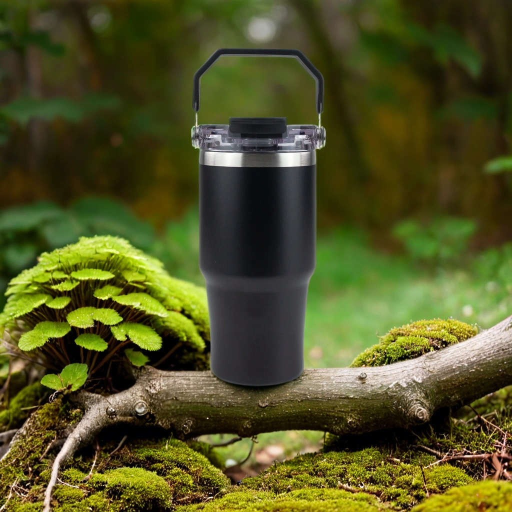 Black insulated tumbler with lid and handle on a mossy log in a forest setting, outdoor gear