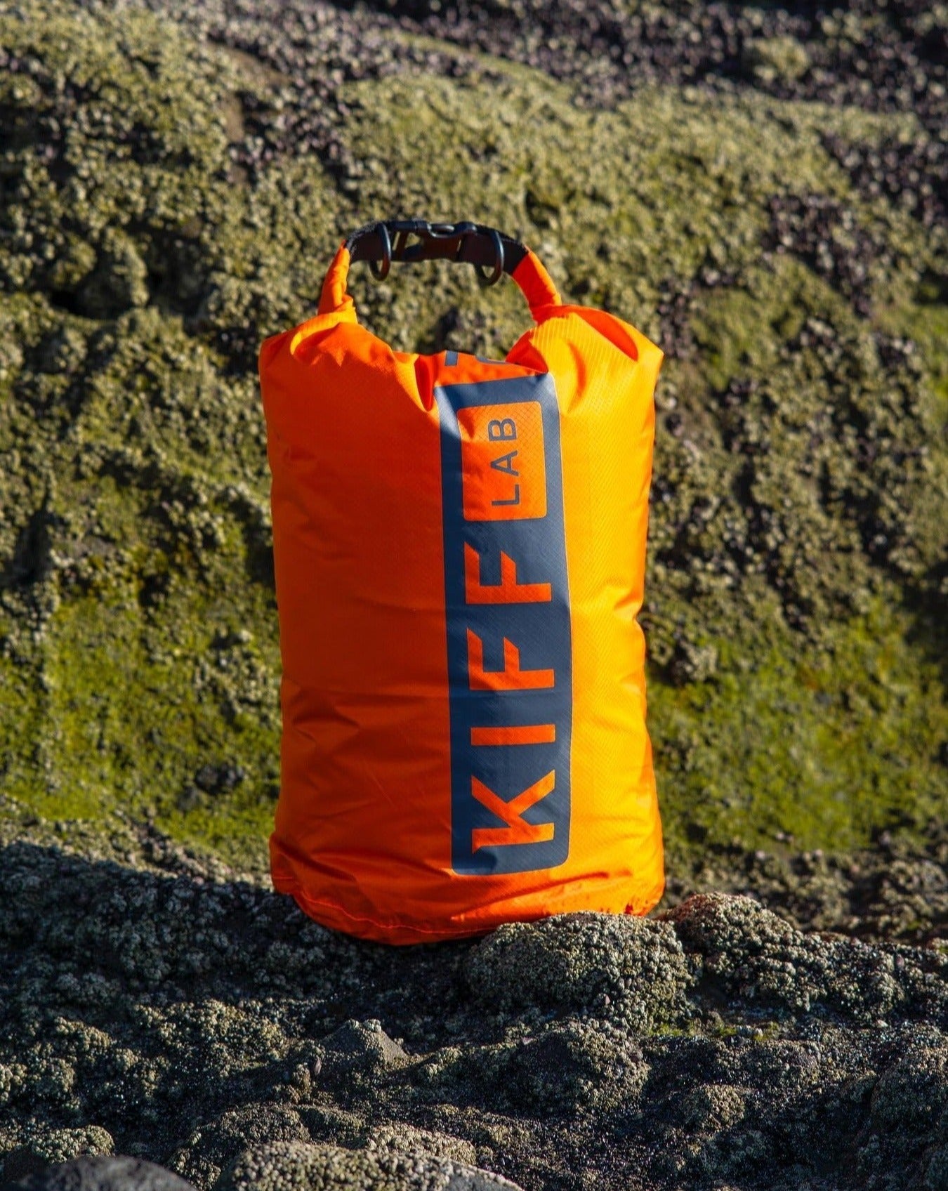 Bright orange dry bag for camping or outdoor gear on rocky, mossy terrain