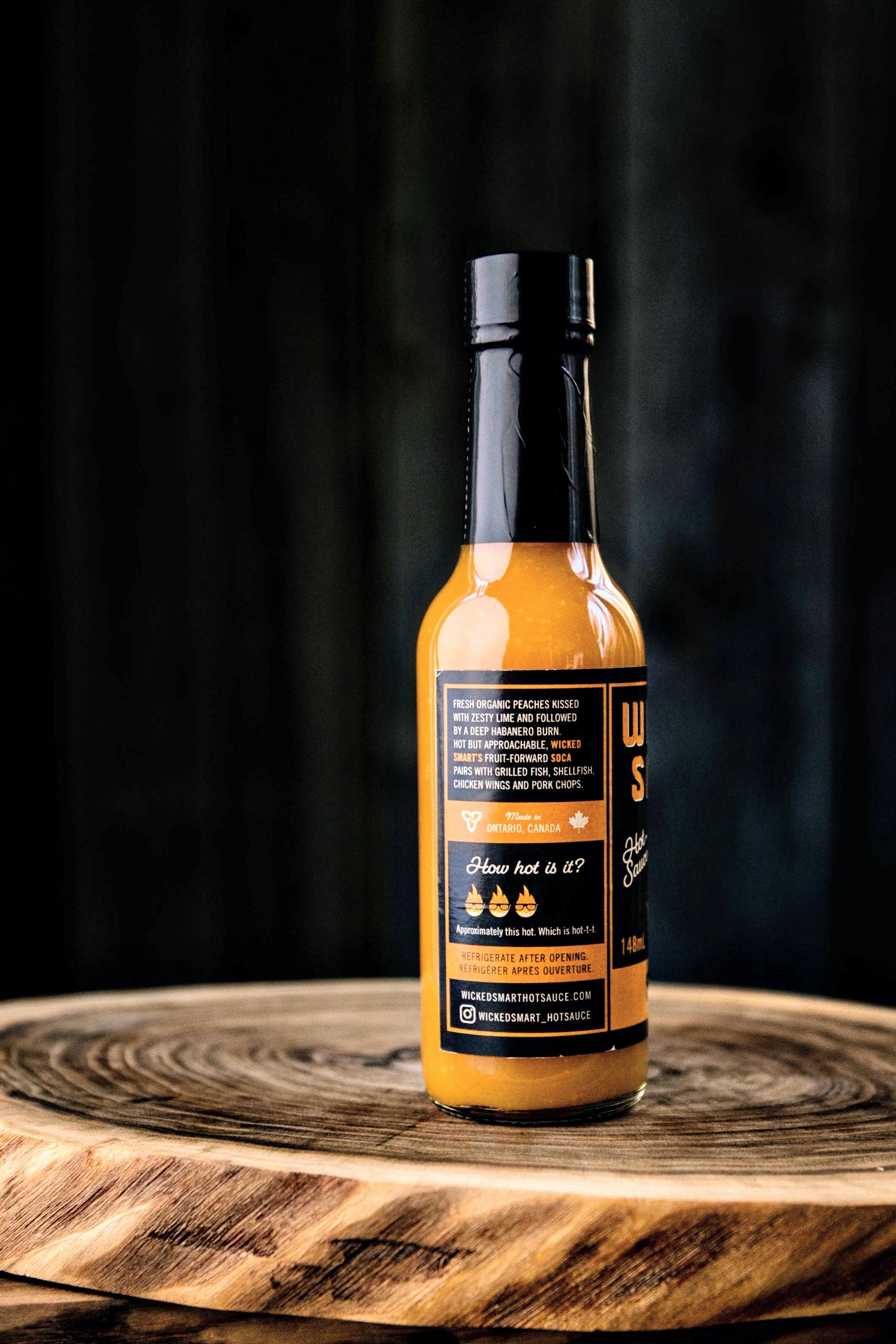 Hot sauce bottle with orange sauce on wooden board, label showing heat level and ingredients.
