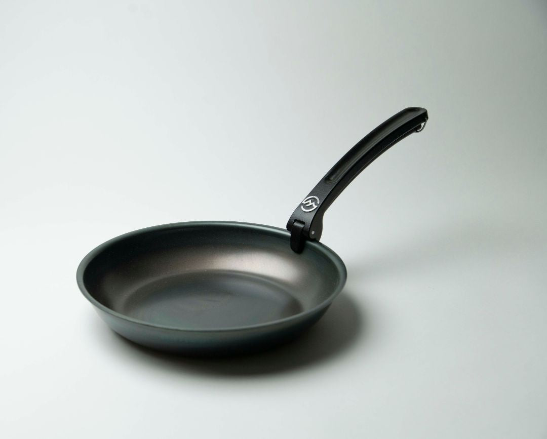 Non-stick frying pan with detachable black handle on light background, camping cookware