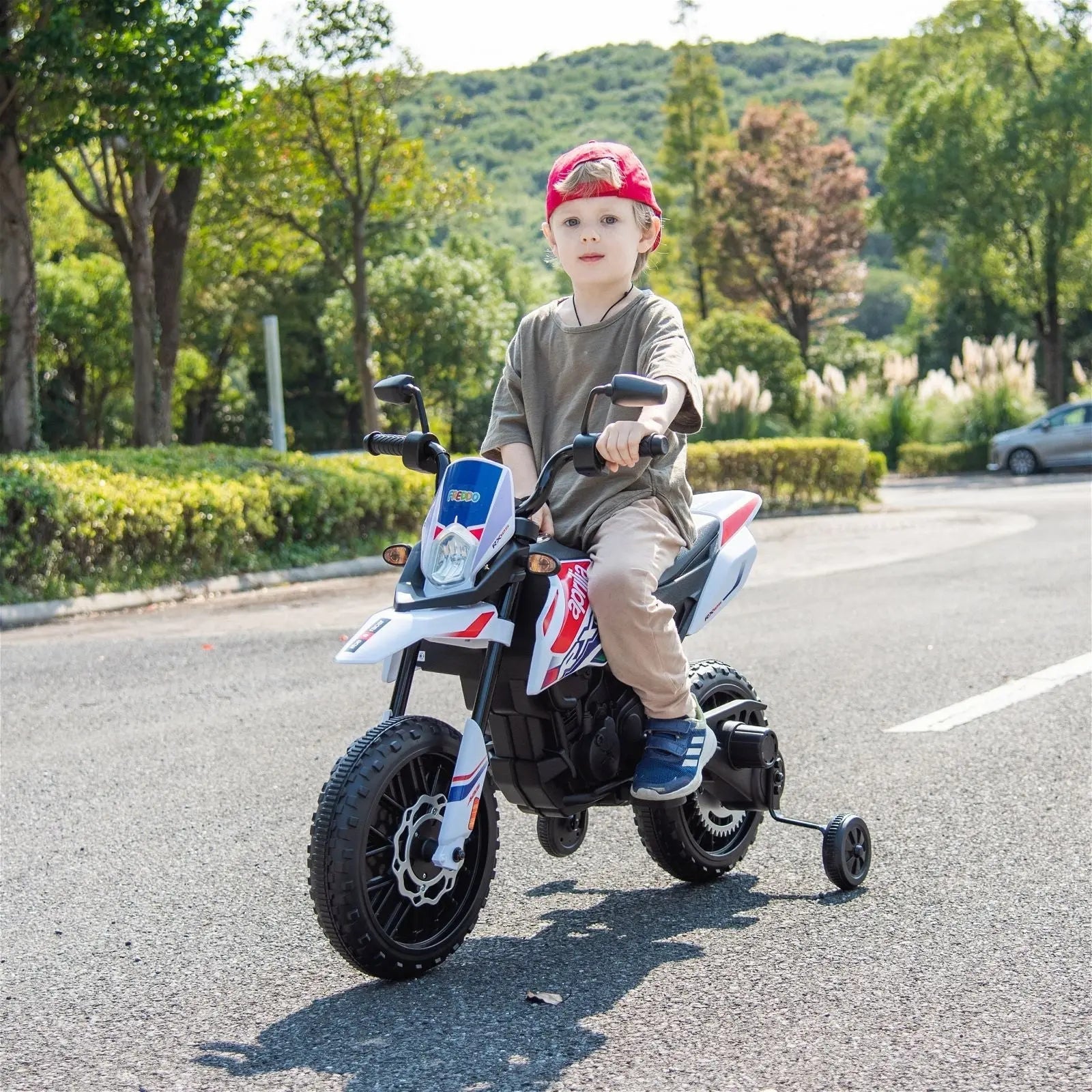 Child riding a 12V Aprilia kids electric motorcycle with training wheels outdoors