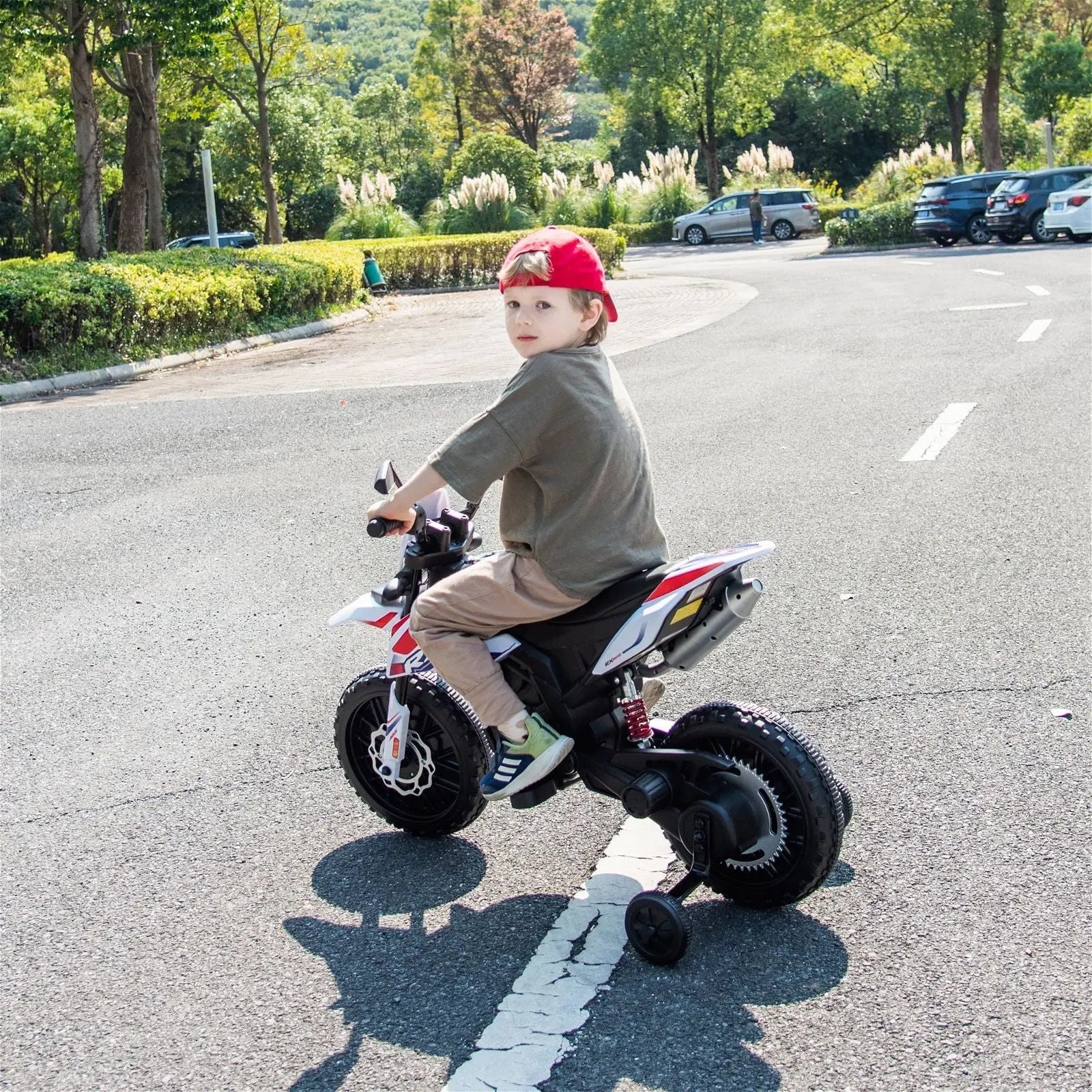 Child riding a red and white electric toy motorcycle on an outdoor road