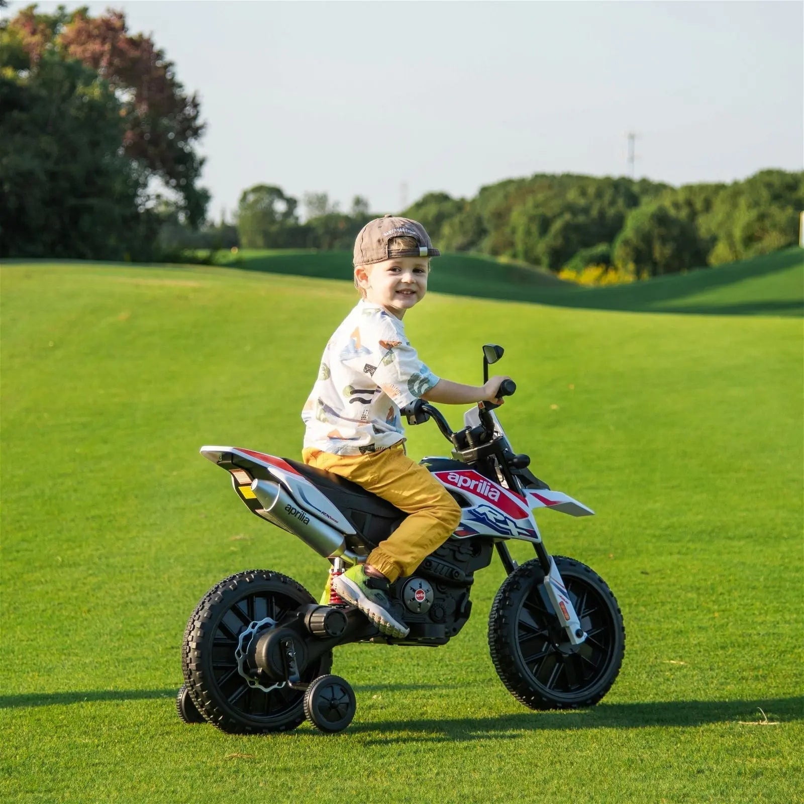 Child riding 12V Aprilia ride-on motorcycle for kids outdoors on green grass